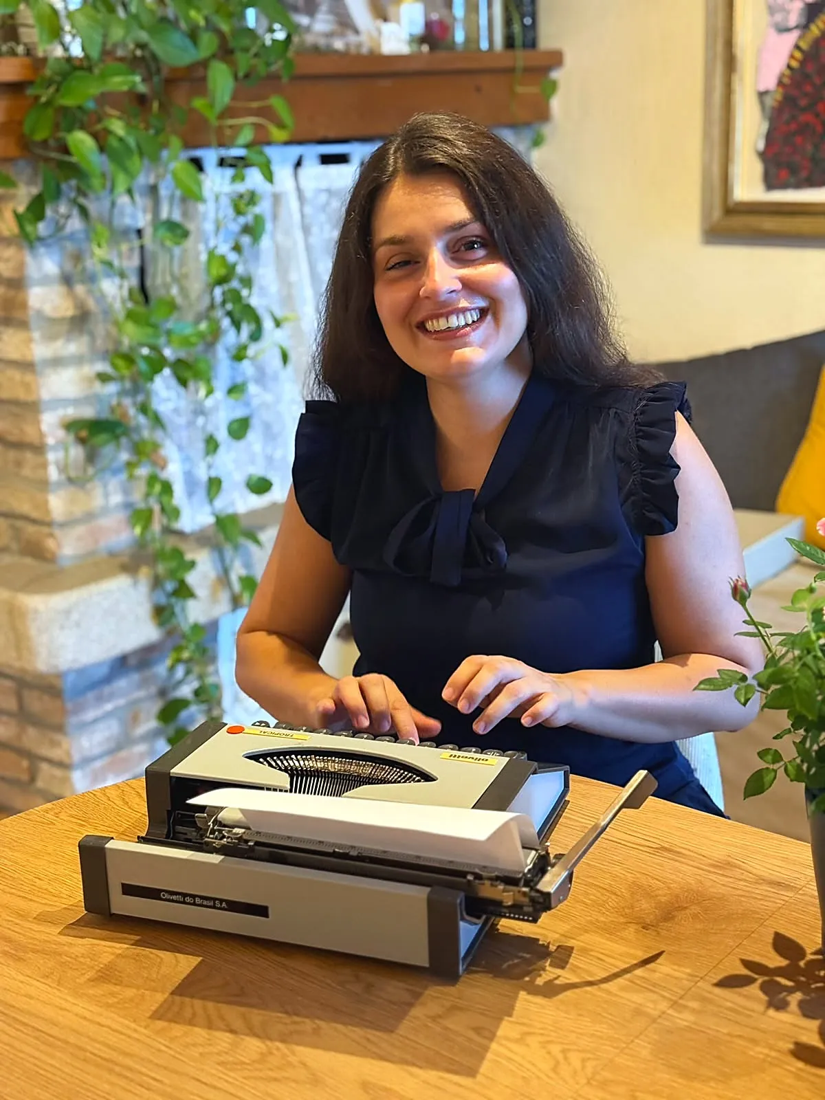 Valentina Alberti sorridente, seduta al tavolo con una macchina da scrivere Olivetti d'epoca